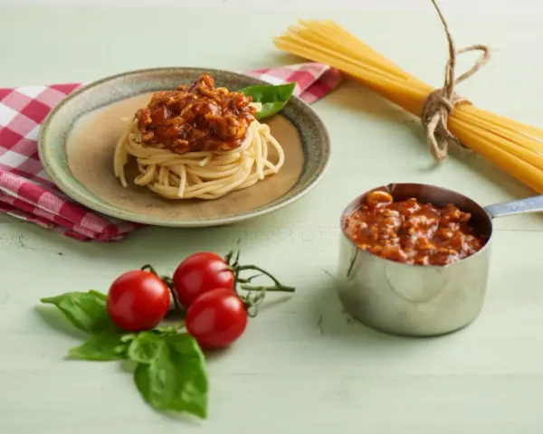 Pyszny sos do spaghetti z mięsem mielonym, podany na talerzu z makaronem, obok świeżych pomidorków i bazylii.