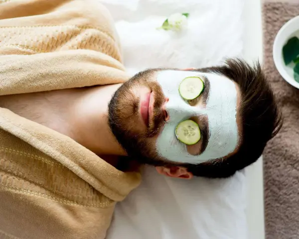 Man with a face mask and cucumber slices on eyes, relaxing. Wondering how long to keep face mask on for best results.