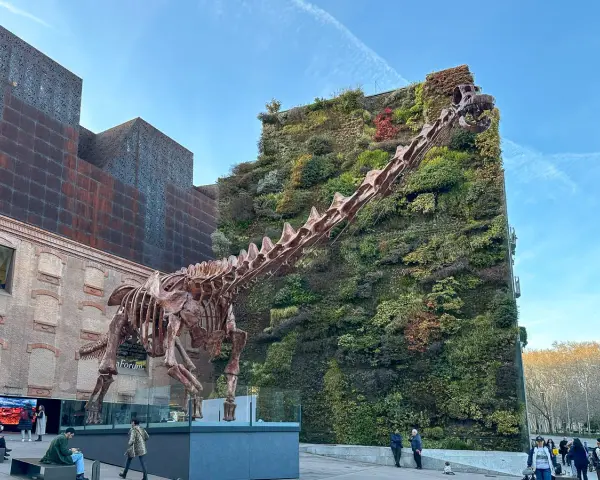 Szkielet dinozaura przed zieloną ścianą budynku. Madryt nietypowe atrakcje, które zaskakują.