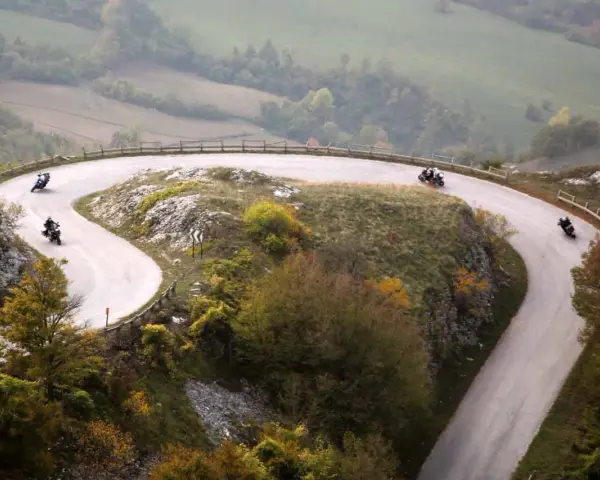 Motociclisti sfrecciano sulle curve delle Gole del Furlo, immersi in un paesaggio autunnale.