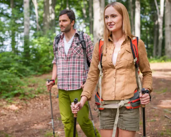 Ein Paar wandert achtsam durch einen Wald. Die Frau und der Mann nutzen Wanderstöcke, eine Anleitung für einen achtsamkeitsspaziergang.