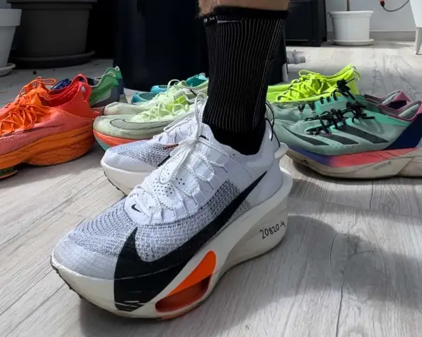 En person visar upp sina löparskor, redo för hoka halvmaraton. Flera färgglada skor ligger utspridda på golvet.