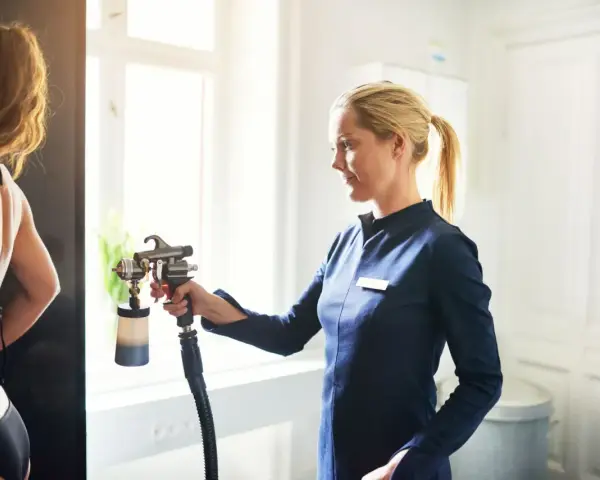 Profesjonalne opalanie natryskowe: jak długo się utrzymuje? Stylistka z pistoletem do opalania w dłoni.