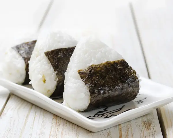 Trzy ryżowe kulki onigiri z nori na białym talerzyku. Idealne na szybki lunch, oto prosty onigiri przepis.