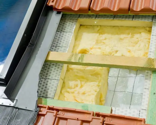 Wełna mineralna to świetny wybór, czym najlepiej ocieplić dom. Widoczna jest jej instalacja pod dachówką.