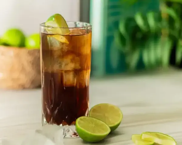 Orzeźwiający Cuba Libre, czyli rum z colą i limonką, z kostkami lodu i świeżymi limonkami w tle. Idealny na upalne dni.