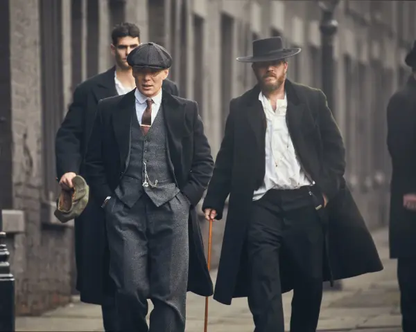 Tommy Shelby e altri uomini in abiti eleganti camminano per strada.