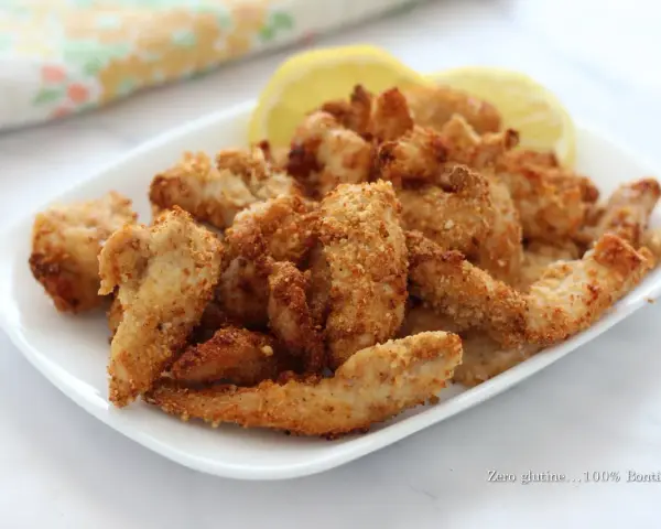 Straccetti di pollo in friggitrice ad aria, dorati e croccanti, serviti su un piatto bianco con spicchi di limone.
