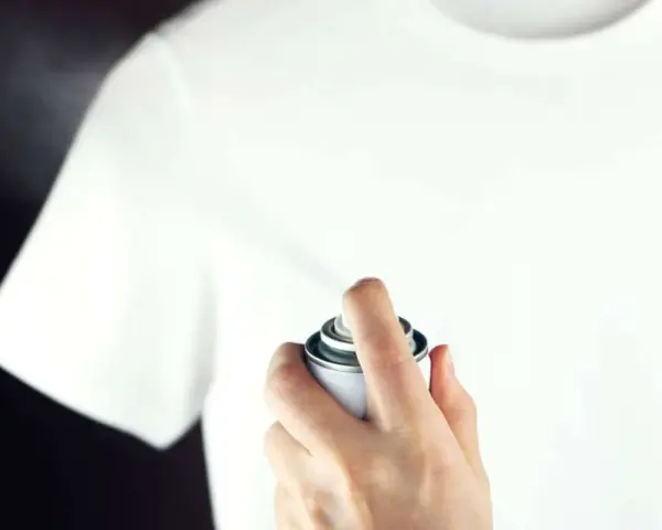 Hand sprüht mit einer Dose auf ein weißes T-Shirt, um statische Aufladung zu verhindern.