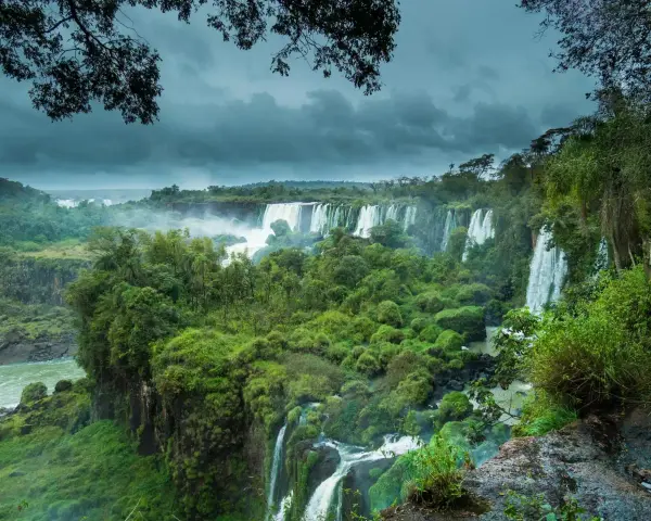 Majestuosas cataratas del Iguazú, un torrente de agua cayendo entre exuberante vegetación bajo un cielo nublado.