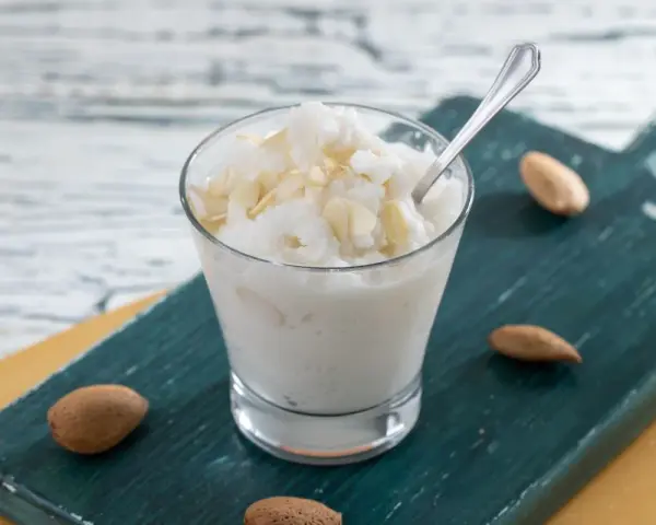 Rinfrescante granita alla mandorla, guarnita con lamelle di mandorle, servita in un bicchiere su un tagliere scuro.