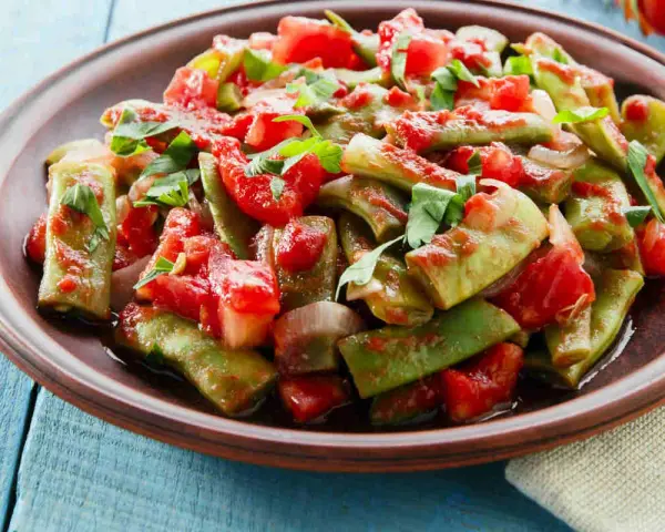 Piatto di taccole al pomodoro, condite con cipolla e prezzemolo fresco, servite su un piatto di terracotta.