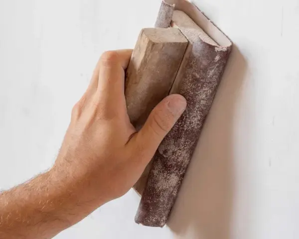 Mano lijando una pared con lija para pared y bloque de madera.