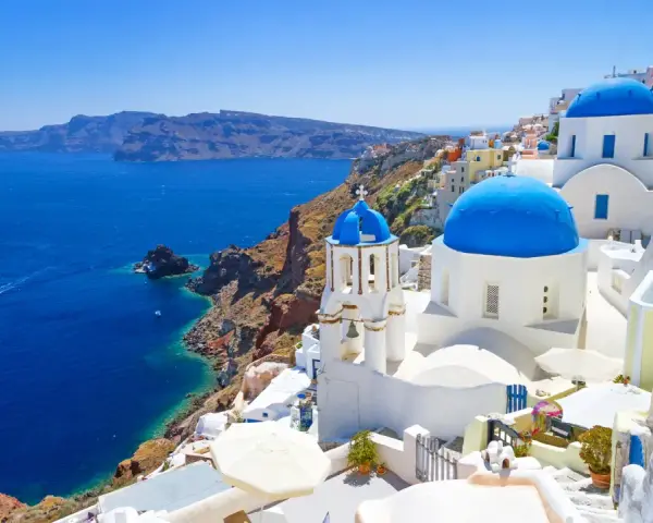 Santorini wycieczki: białe domy z niebieskimi kopułami na klifie nad błękitnym morzem. Statek płynie w oddali.
