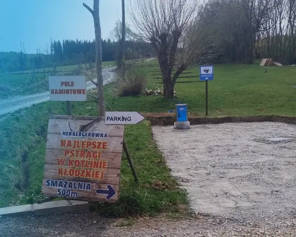 Miejsce na parking dla kamperów. Obok znak "Pole Namiotowe" i drogowskaz do smażalni pstrągów.