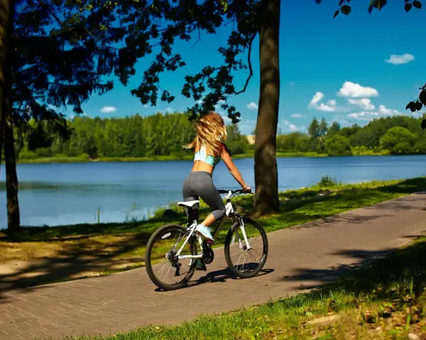 Kobieta na rowerze przemierza malownicze **trasy rowerowe Mazury** wzdłuż jeziora.