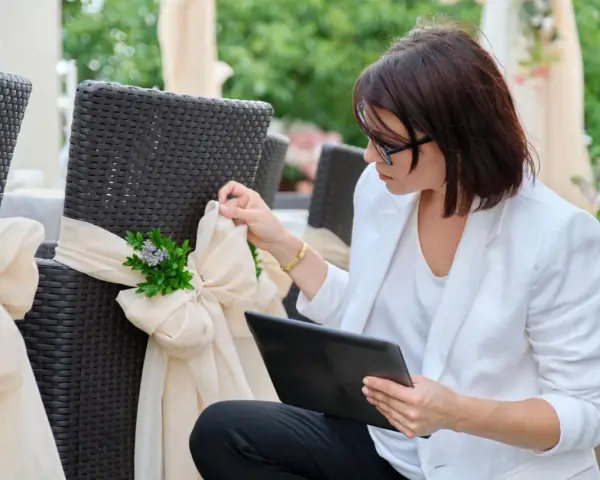 Kobieta w białej marynarce dopina wstążkę na krześle. Czy warto wynająć wedding plannera na samą koordynację dnia ślubu?
