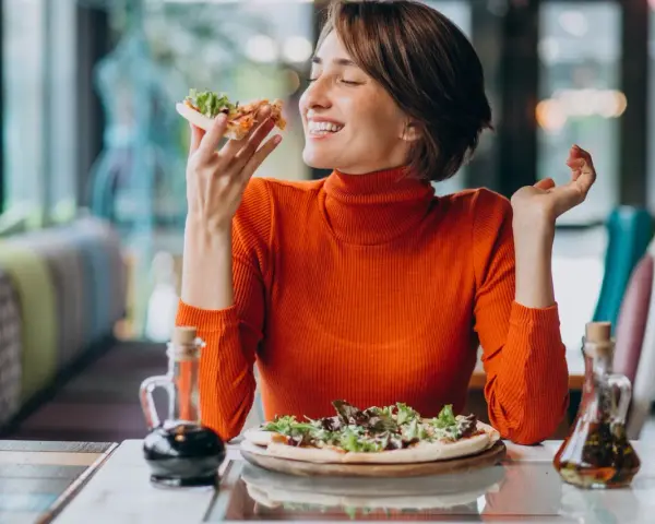Kobieta w pomarańczowym golfie cieszy się pizzą, czując radość. W czym jest serotonina? W takich chwilach szczęścia!
