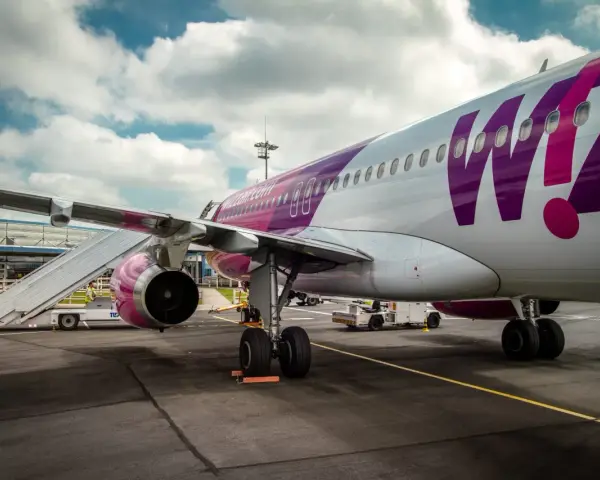 Samolot Wizz Air z fioletowym logo na lotnisku, z drabiną przy skrzydle.