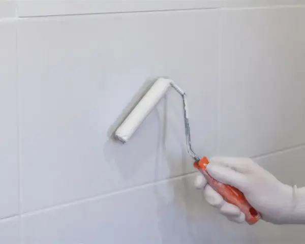 Mano enguantada pintando con rodillo blanco sobre azulejos grises. Renovando el aspecto de los tubos calefacción.