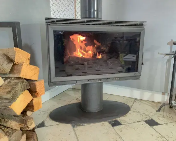 Un poêle à bois avec une vitre propre pour changer une vitre de poele a bois. Des bûches de bois sont empilées à gauche.