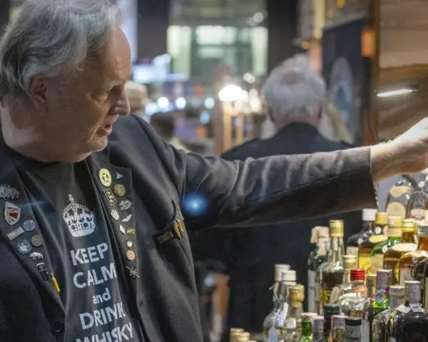 Mann mit "Keep Calm and Drink Whisky"-Shirt und vielen Ansteckern auf einer Whiskey Messe, der eine kleine Box hält.