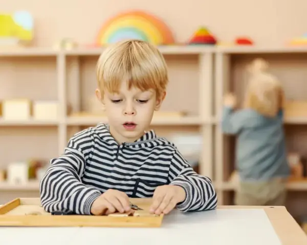 Chłopiec skupiony na zadaniu z materiałem Montessori. Ta metoda polega na samodzielnym odkrywaniu świata przez dziecko.