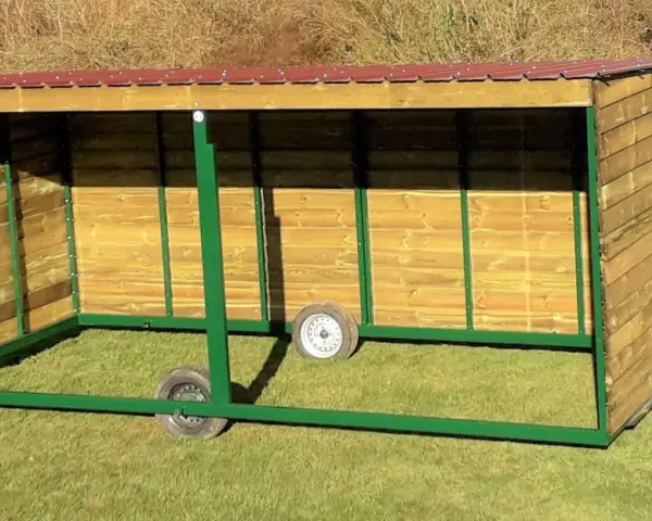 Abri pour chevaux en bois, mobile et sans permis de construire, avec toit rouge et structure verte.