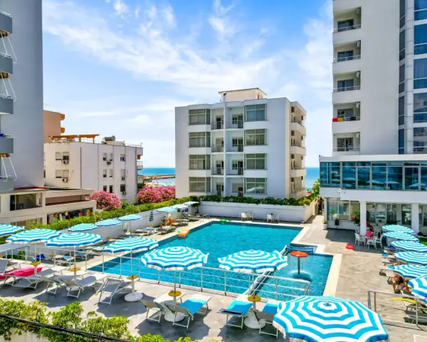 Albania - wczasy samolotem all inclusive. Basen hotelowy z leżakami i parasolami, w tle budynki i morze. Idealne miejsce na relaks.