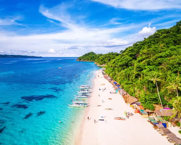 Rajska plaża na Filipinach z turkusową wodą, białym piaskiem, łodziami i zielonymi wzgórzami.