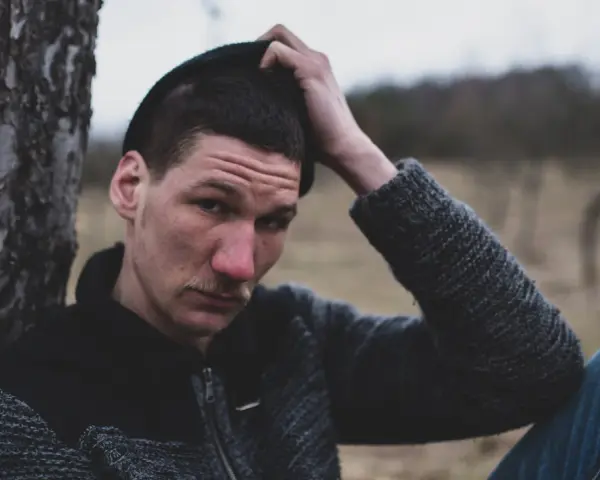 Quebonafide w czapce i swetrze, oparty o drzewo. W tle jesienny krajobraz. Tekst "żadnych zmartwień" pasuje do nastroju.
