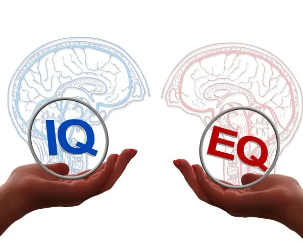 Dwie dłonie trzymają symbole IQ i EQ, symbolizujące równowagę między inteligencją a inteligencją emocjonalną.