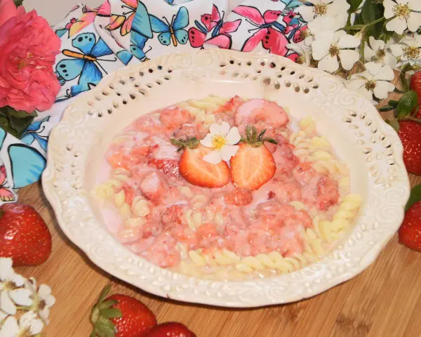 Makaron fusilli z sosem truskawkowym, udekorowany połówkami truskawek i kwiatkiem.