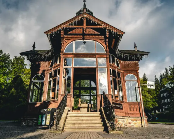 Drewniany pawilon w Karlovej Studance, ozdobiony lampkami, zaprasza do środka. Wspaniała architektura i otoczenie lasu tworzą magiczną atmosferę.