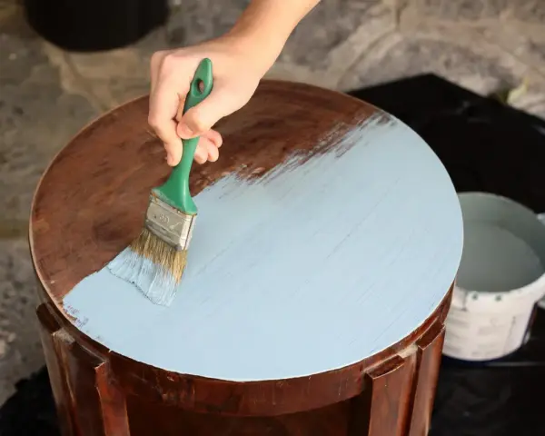 Mano aplicando pintura a la tiza color madera a una mesa redonda.