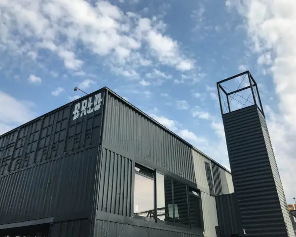 Moderne Containerarchitektur am **brlo gleisdreieck** mit Schriftzug "BALD" und einem markanten Turm unter blauem Himmel.