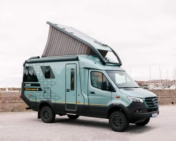 En grön Hymer Venture S husbil med uppfällt tak står parkerad vid en hamn.