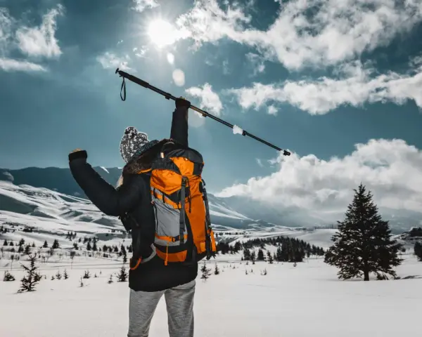 Osoba z plecakiem wznosi kijek, przygotowując się do marszu. Dowiedz się, jak prawidłowo założyć buciki na kijki nordic walking, by cieszyć się zimową wędrówką.