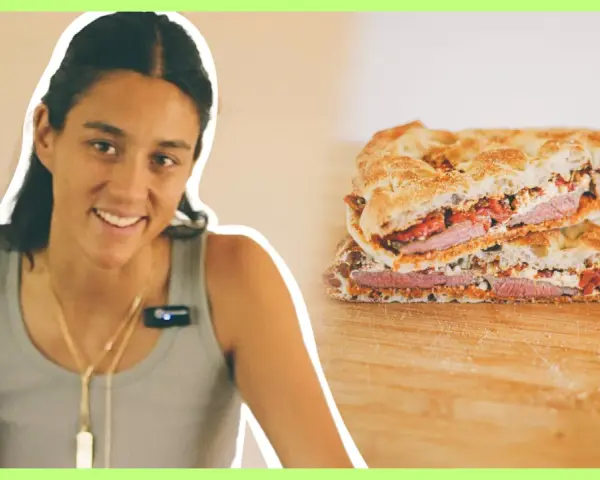 Mujer sonriente junto a un pepito de ternera cortado en dos, mostrando el relleno de carne, queso y pimientos.