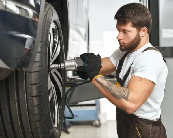 Meccanico con guanti neri lavora su una ruota. Per sapere ogni quanto girare le gomme, consulta il manuale dell'auto.