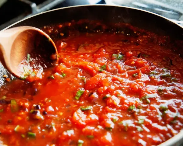 Gęsty, aromatyczny sos do spaghetti gotuje się na patelni. Drewniana łyżka miesza pomidorową masę z ziołami.