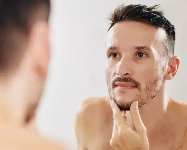 Mężczyzna zastanawia się, jak zagęścić brodę, dotykając jej palcami przed lustrem.