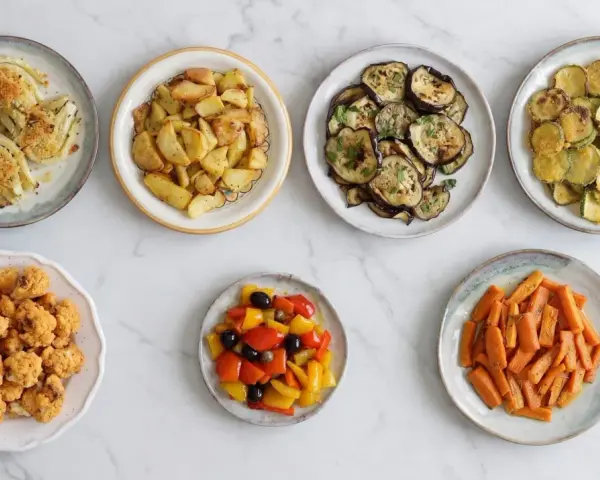 Sette piatti di verdure in friggitrice ad aria: finocchi, patate, melanzane, zucchine, cavolfiore, peperoni e carote.
