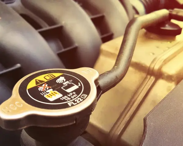 A car's radiator cap, showing warnings about hot coolant. A faulty cap can cause overheating, one of the bad radiator cap symptoms.