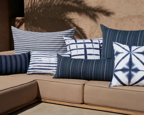 Idée déco plaid sur canapé : coussins bleus et blancs aux motifs rayés et tie-dye sur un canapé de jardin.