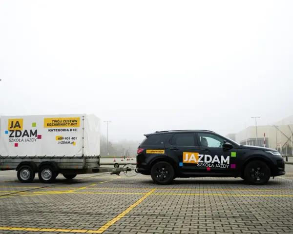 Czarny SUV z przyczepą szkoleniową "JA ZDAM" na placu manewrowym. Zestaw do kategorii B+E gotowy do egzaminu.