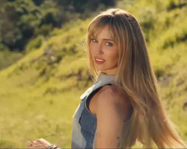 Miley Cyrus w nowej piosence, w letniej stylizacji, na tle zielonych wzgórz.