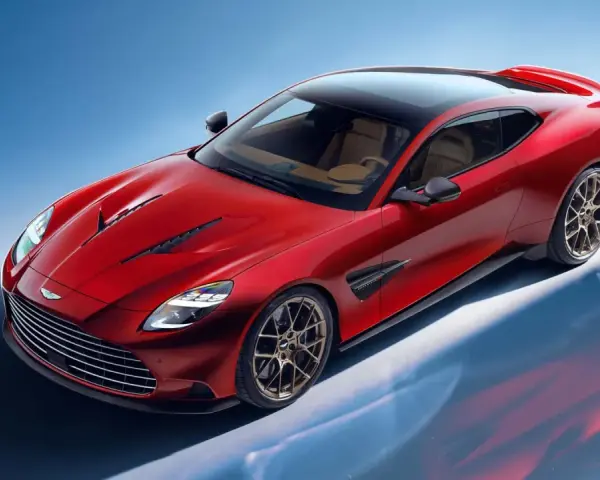Czerwony Aston Martin Vanquish z brązowym wnętrzem i czarnym dachem, prezentujący swoje sportowe linie na tle błękitnego nieba.