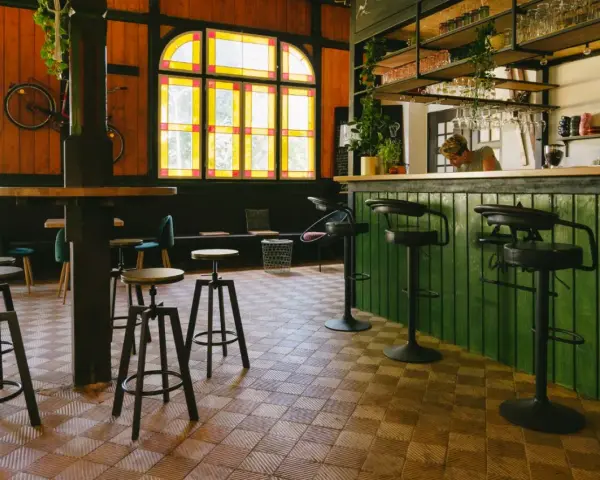 Wnętrze kawiarni z zielonym barem, stołkami i rowerem na ścianie. Idealne miejsce na coffee ride.