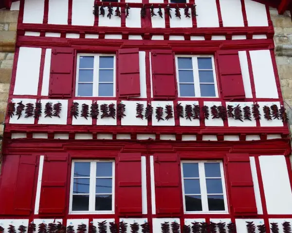 Façade rouge et blanche typique d'Espelette, avec des piments séchant. Combien de temps pour visiter Espelette ? Une journée suffit pour admirer ce village pittoresque.